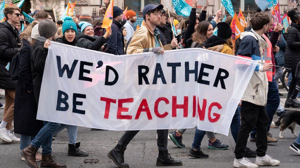 Why are teachers striking? here is an image of several teachers in protest holding the signs 'We'd rather be teaching'